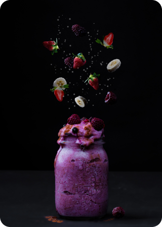 Copo em cima de uma mesa com milkshake roxo e várias frutas em cima